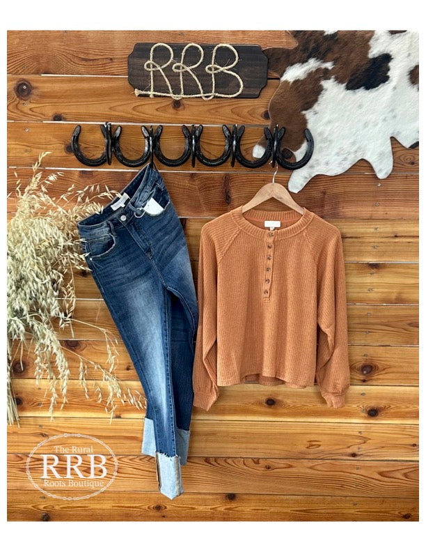 Introducing The Loomis Long Sleeve Henley Knit Top in a warm light rust hue. This stylish top features a button-down Henley neckline and extended shoulder design for a relaxed, modern look. Made from a comfortable blend of 80% polyester, 16% rayon, and 4% spandex, it ensures a soft and flattering fit. Available in Small (2-4), Medium (6-8), and Large (8-10), it's perfect for pairing with the Laramie High Rise Cuffed Straight Leg Jeans for a chic, laid-back outfit.
