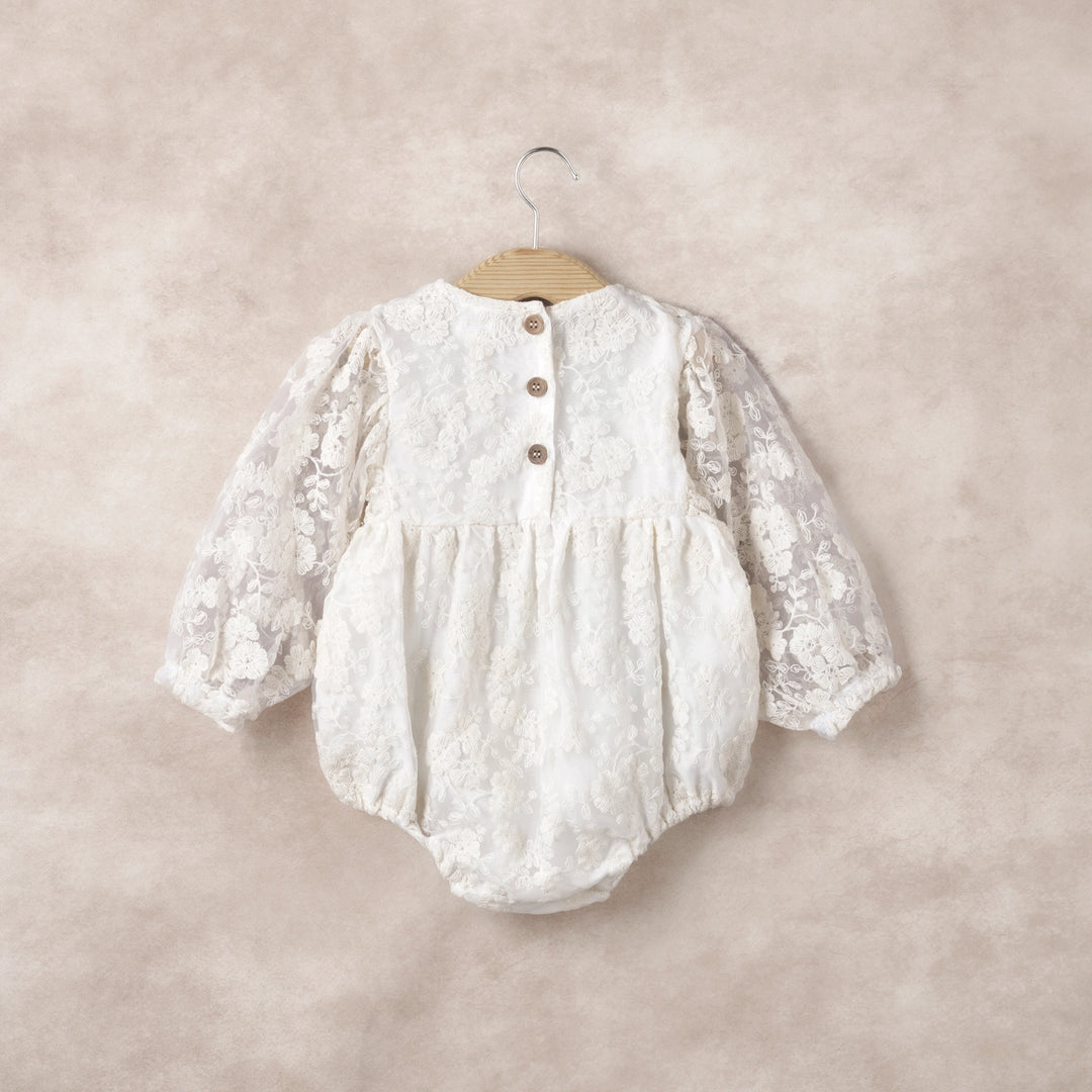 Celebrate your little one in style with the Lace Romper, a dreamy blend of elegance and comfort. The sheer ivory organza overlay is embroidered with intricate detailing, creating a refined, vintage-inspired silhouette that elevates any special occasion. Long sleeves with soft elastic cuffs keep baby cozy while adding subtle sophistication, and thoughtful back buttons with snaps underneath make dressing and diaper changes effortless. Lightweight, breathable, and designed for ease of movement, this romper bal