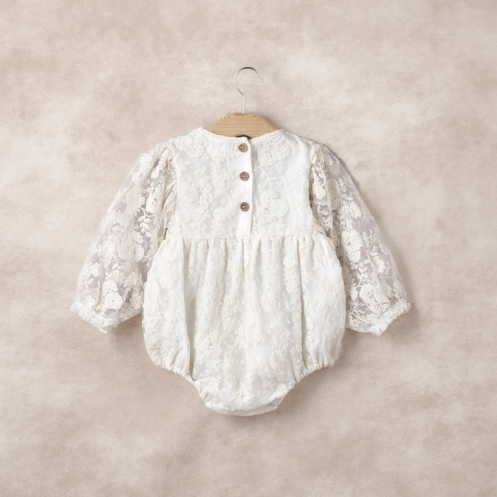 Celebrate your little one in style with the Lace Romper, a dreamy blend of elegance and comfort. The sheer ivory organza overlay is embroidered with intricate detailing, creating a refined, vintage-inspired silhouette that elevates any special occasion. Long sleeves with soft elastic cuffs keep baby cozy while adding subtle sophistication, and thoughtful back buttons with snaps underneath make dressing and diaper changes effortless. Lightweight, breathable, and designed for ease of movement, this romper bal
