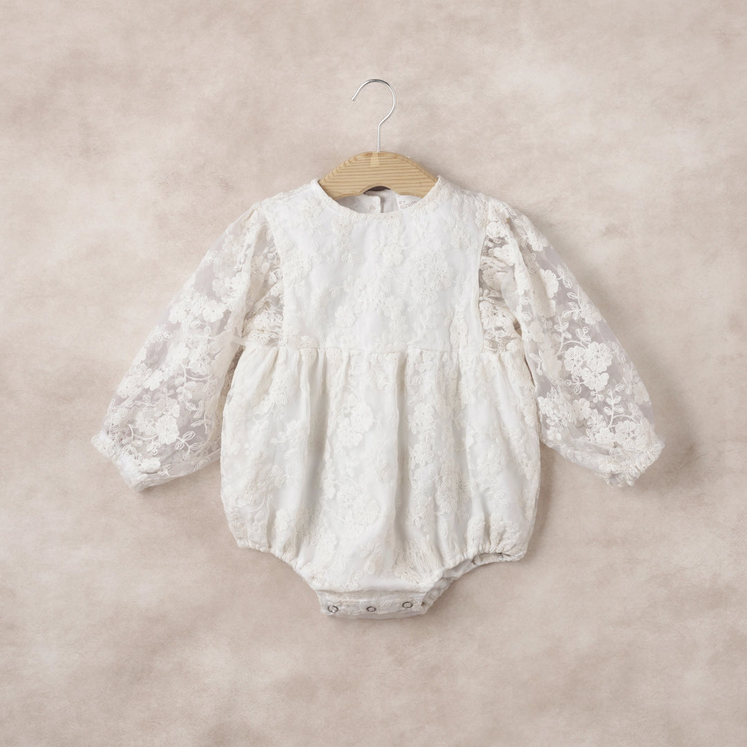 The Lace Romper brings a touch of timeless elegance to your baby’s wardrobe. Featuring a delicate sheer organza overlay with intricate embroidery in soft ivory, this romper creates a refined and graceful silhouette perfect for christenings, weddings, family portraits, or other special occasions. Long sleeves with gentle elastic cuffs provide both comfort and charming detail, allowing your little one to move freely while maintaining a polished look. Thoughtfully designed with back buttons and bottom snaps, t