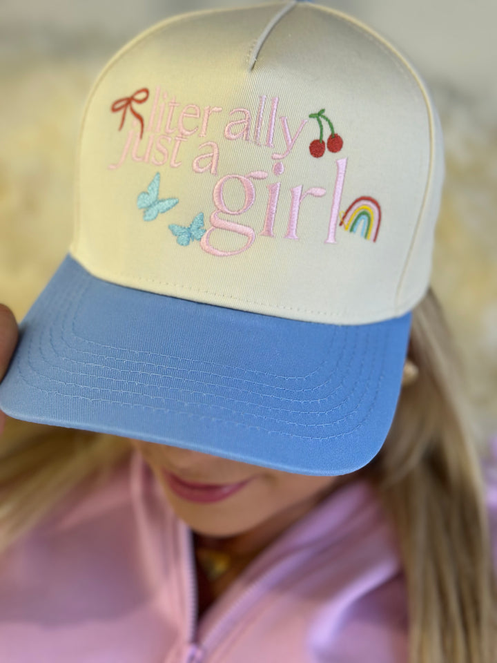 The Literally Just A Girl Cap features a blue and natural canvas design with an adjustable snapback closure and embroidered lettering, perfect for a casual, laid-back look.