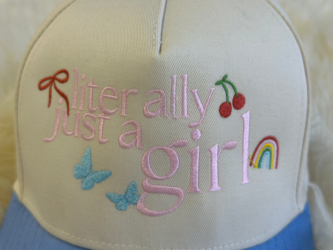 The Literally Just A Girl Cap in blue and natural canvas offers a stylish embroidered design with an adjustable snapback fit for all-day comfort and effortless style.