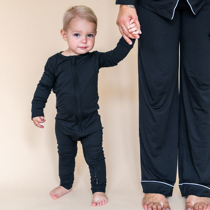 The Allie black bamboo footie features white foot accents and ultra soft bamboo viscose fabric gentle on baby skin perfect for sleep or play this cozy eco friendly baby sleeper keeps little ones comfortable all year long and easy to wash.