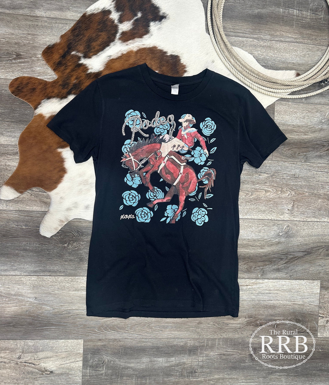 Embrace Western style with The Bronc Rider Rose Shirt in black, featuring a hand-drawn graphic by XOXOart & Co. Made from 100% cotton, this unisex graphic tee offers a comfortable fit for all body types. Perfect for rodeos, country concerts, or casual outings, it's a stylish addition to any cowboy or cowgirl's wardrobe.