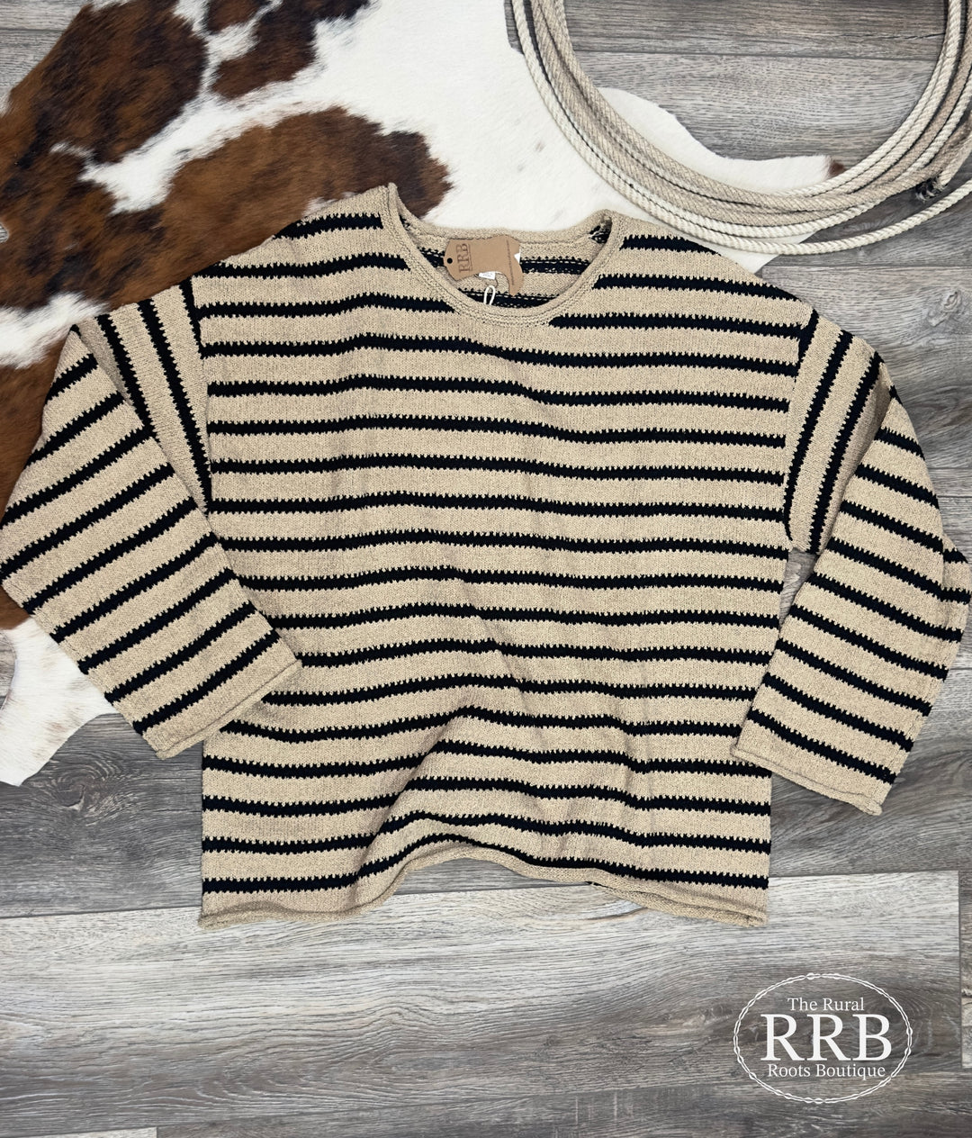 Wrap yourself in The Grove Knit Sweater, showcasing a black and taupe stripe pattern. This pullover features a boat neckline, long drop shoulder sleeves, and raw edge accents for a trendy look. Crafted from a comfortable 75% acrylic and 25% polyester blend, this sweater is perfect for any occasion. Available in Small, Medium, and Large.