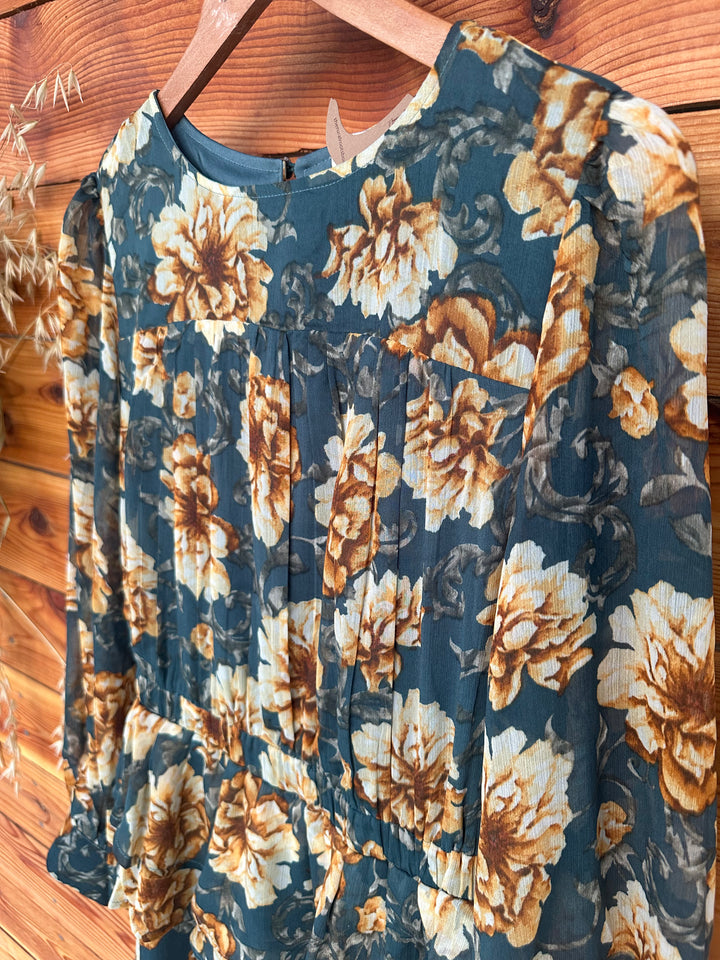 Stylish The Lola teal floral print chiffon dress featuring a layered skirt design, round neckline, and keyhole back with button closure. This dress includes long sleeves with buttoned cuffs, pleated shoulders, and an elastic waist for added comfort. Fully lined and made from 100% polyester, available in sizes Small (3-5), Medium (6-8), and Large (9-11). A chic alternative to similar dresses from Boohoo and PrettyLittleThing.
