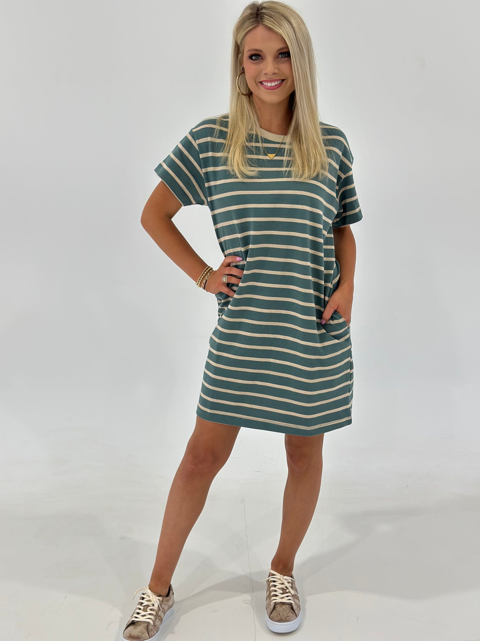 The Looms Striped T-Shirt Mini Dress in Teal/Taupe is made from 100% cotton for a comfortable fit, featuring side pockets and a casual, relaxed vibe. Available in Small (2-4), Medium (6-8), and Large (9-11).