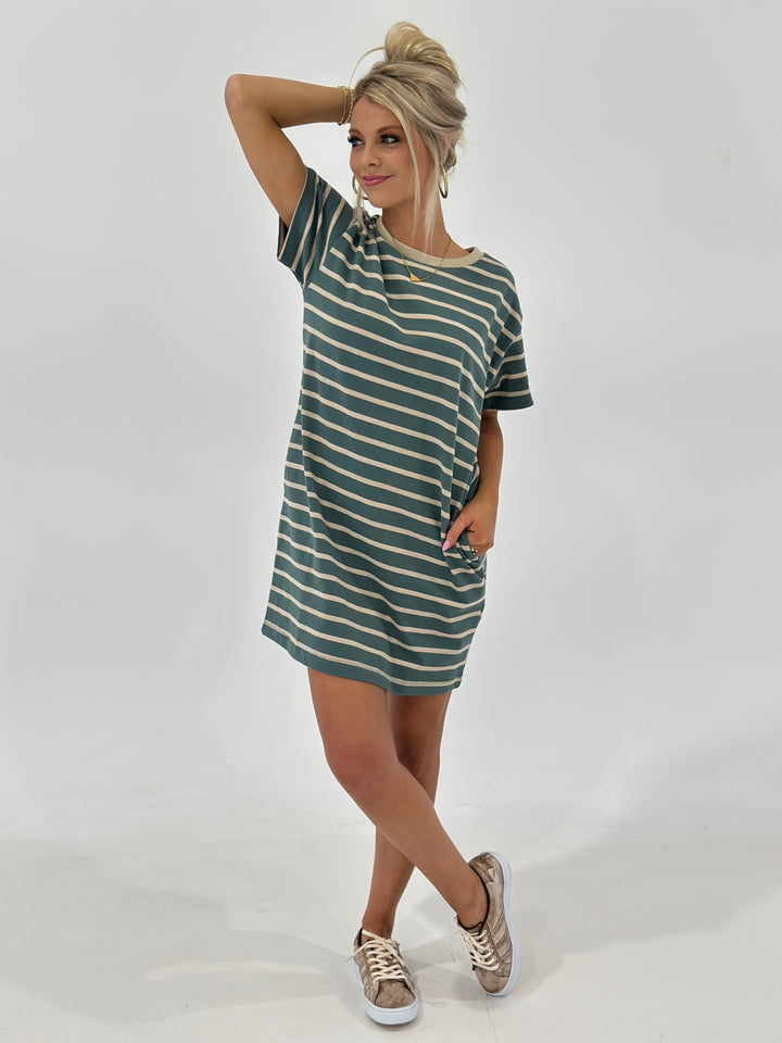 The Looms Striped T-Shirt Mini Dress in Teal/Taupe combines comfort and style with 100% cotton fabric, side pockets, and a flattering fit. Available in Small (2-4), Medium (6-8), and Large (9-11).