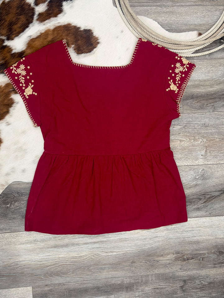 Elegant The Perryn tunic top in wine, showcasing intricate floral embroidery and a stylish square neckline. This short sleeve, non-sheer top is perfect for any occasion. Available in sizes Small (3-5), Medium (6-8), and Large (9-11), it combines fashion with comfort.