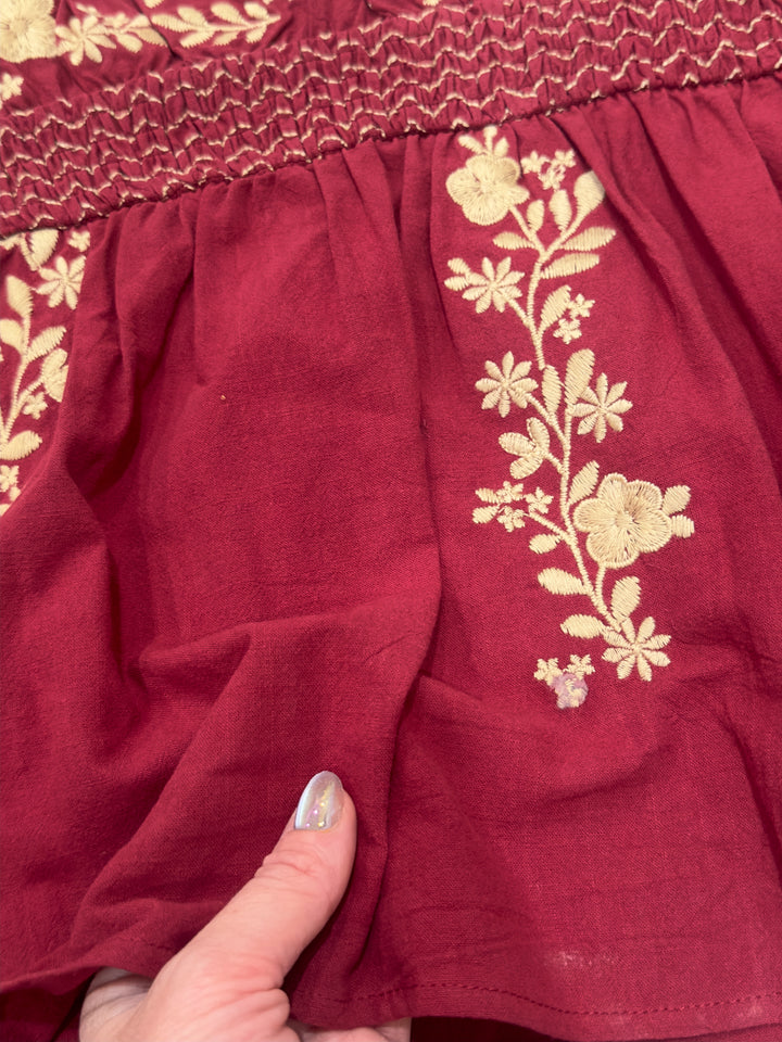 Stylish The Perryn tunic top in a rich wine color, featuring floral embroidery and a square neckline. This short sleeve, non-sheer top is designed for a relaxed fit and available in sizes Small (3-5), Medium (6-8), and Large (9-11), perfect for elevating your everyday look.