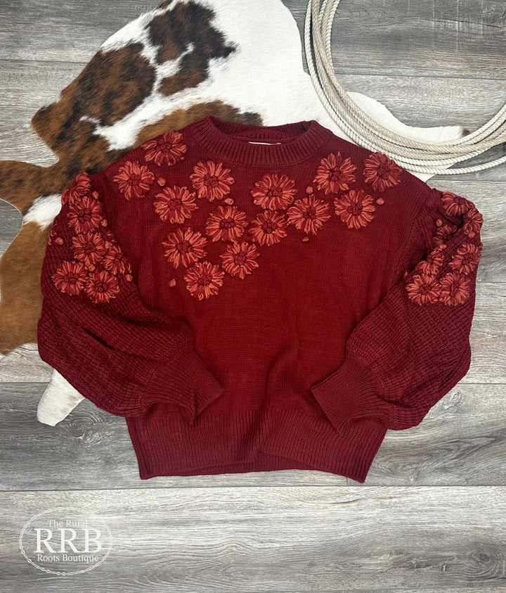 Brighten up your wardrobe with The Ruby sweater in a vibrant crimson hue. This hand-embroidered knit features beautiful flower details, a round neck, and waffle textured long sleeves. The ribbed neck, cuffs, and hem add a touch of style to its relaxed fit. Made from 100% acrylic, it’s available in Small (3-5), Medium (6-8), and Large (9-11).