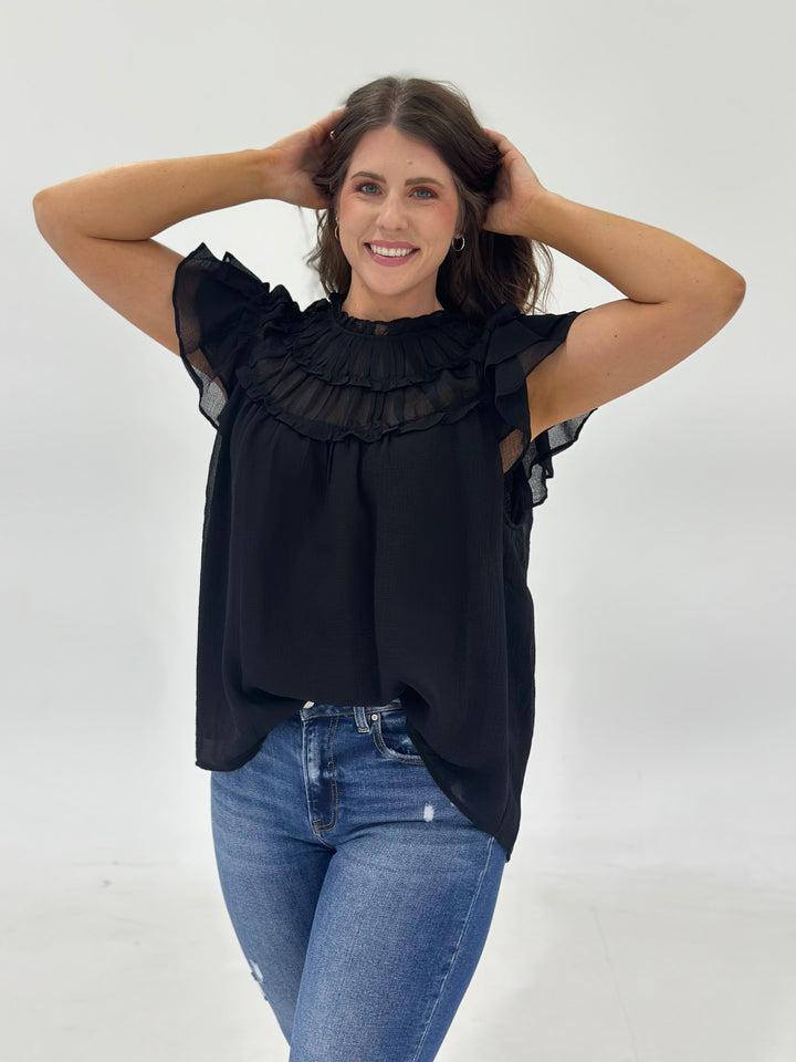 This women’s chiffon blouse features a mock-neck design with soft pleating details at the front, offering an elegant and modern look for everyday wear or professional settings. Designed with short sleeves and a lightweight, lined construction, this solid top provides full coverage with a non-sheer woven fabric that’s both breathable and comfortable. The back features a button closure with a keyhole cutout, adding a subtle feminine touch to the structured silhouette. Ideal for pairing with tailored pants, de
